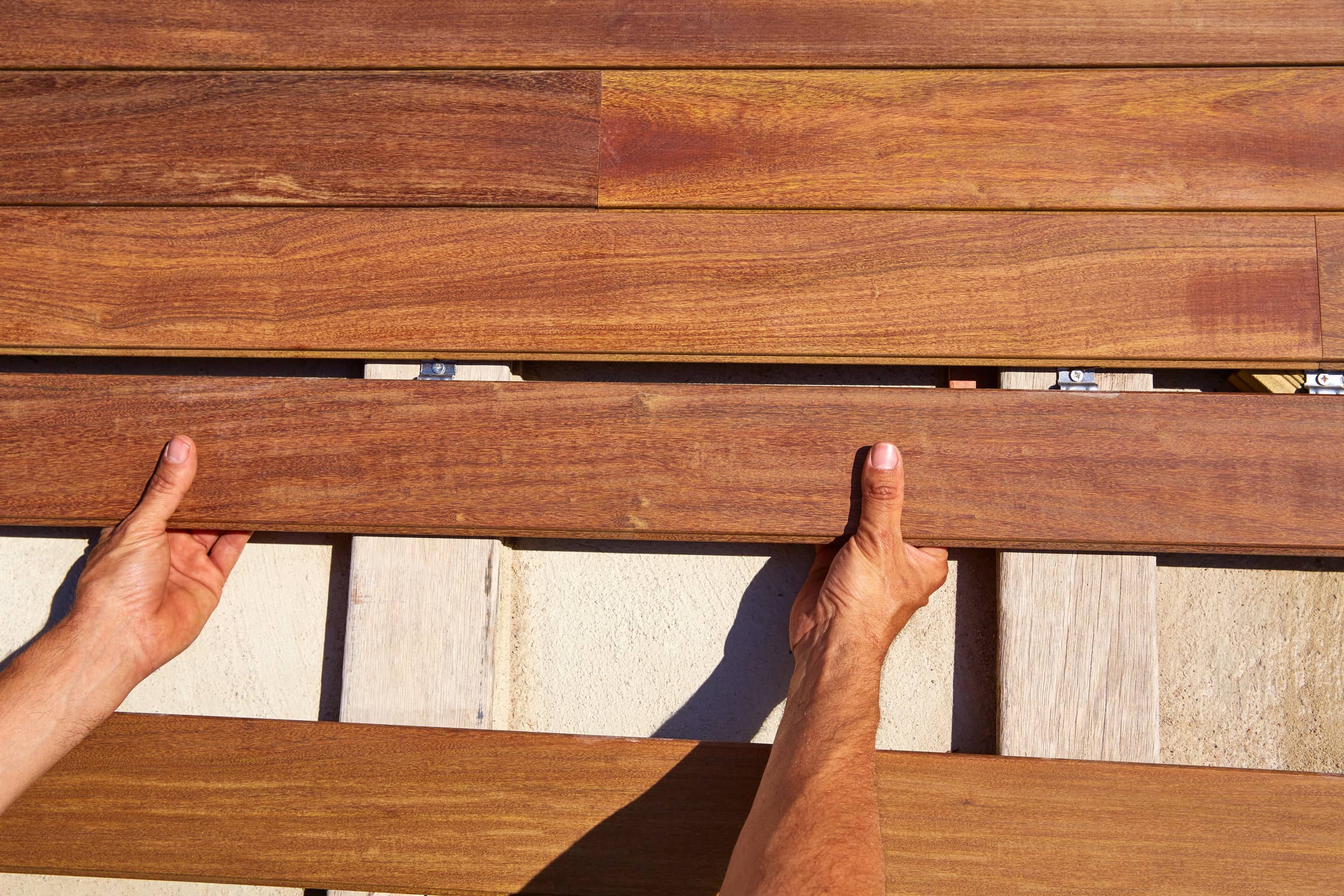 An image of a contractors hands piecing together flooring for a deck.